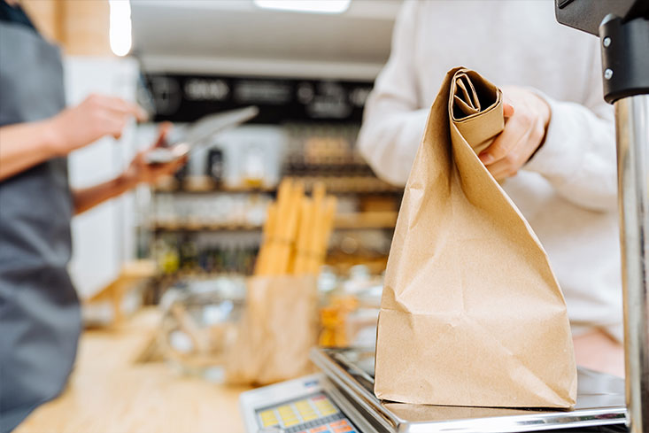 Customer placing a brown paper bag on a digital scale at a zero-waste store counter